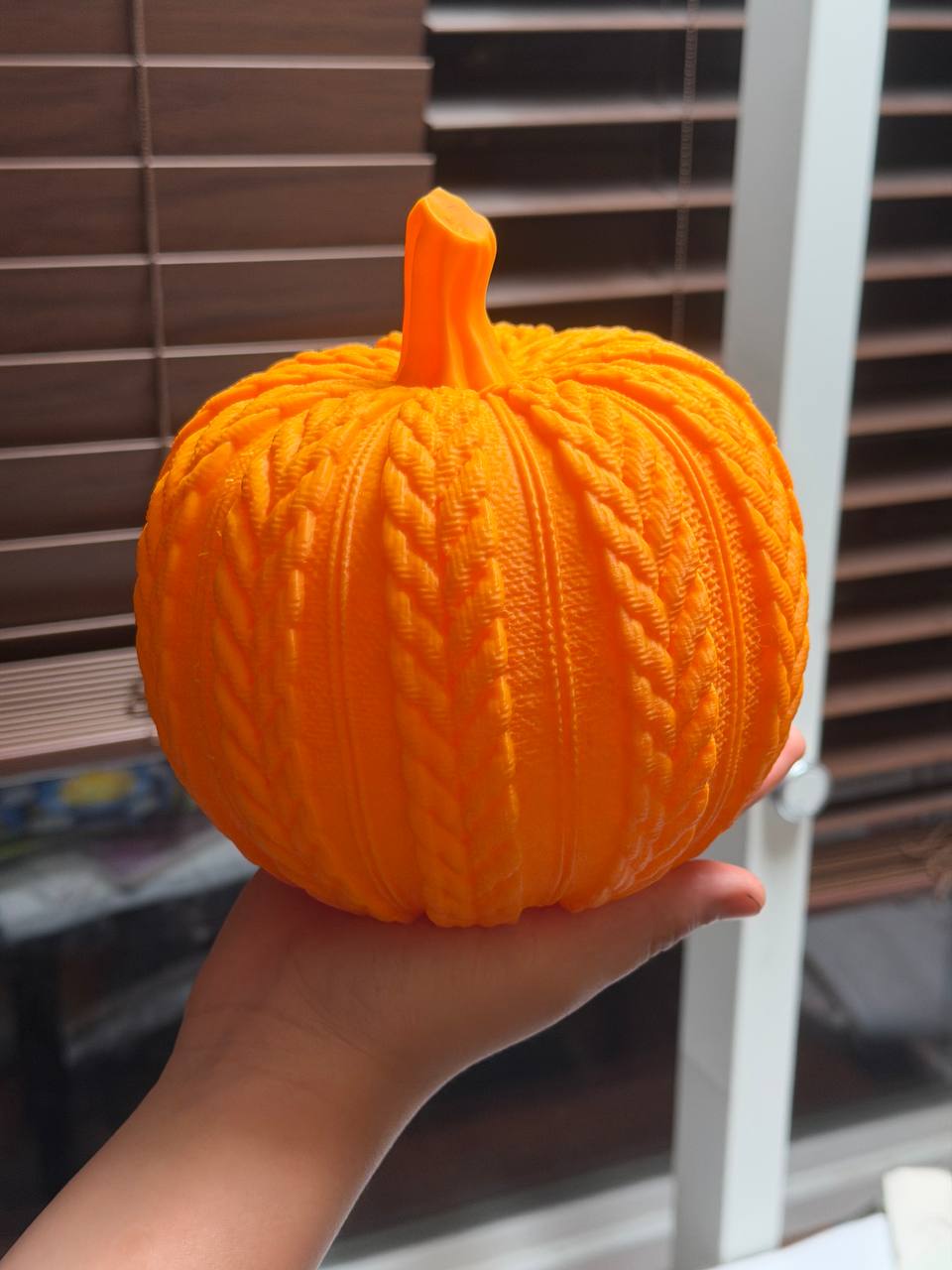 Bright orange 3D printed pumpkin with cable-knit texture held in hand